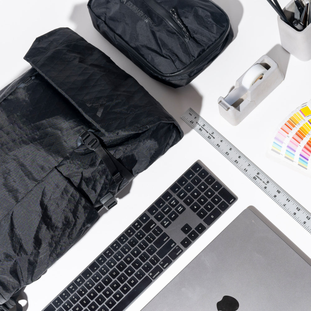Black travel bag, keyboard, laptop, and office supplies on a white surface