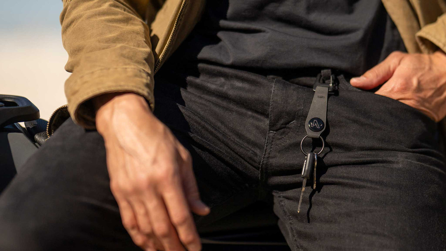 Person wearing black pants with a keychain attached, sitting outdoors.